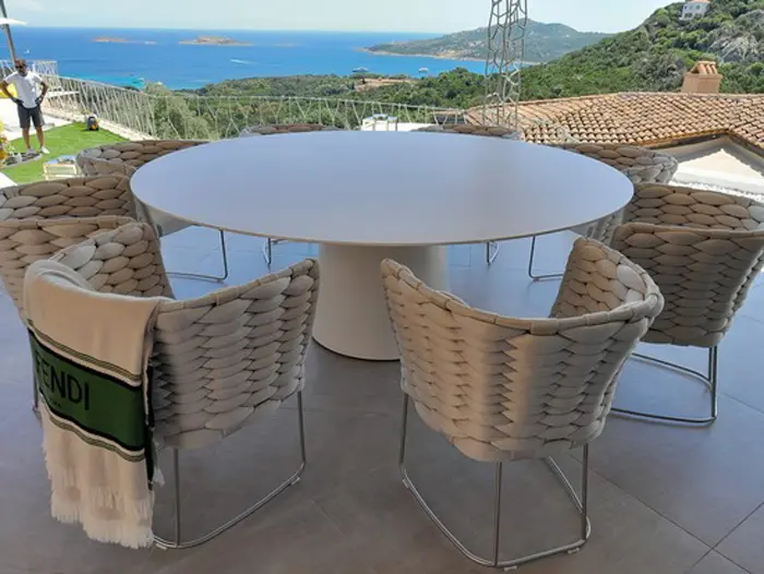 Round white outdoor table with woven chairs on a terrace overlooking the sea