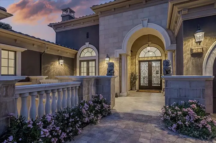 Stone entryway with lion statues, arched wood-and-iron door and blooming pink flowers