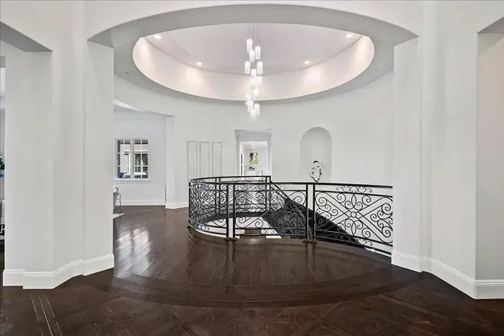 White foyer with a round wrought-iron staircase landing and dark wood herringbone floor