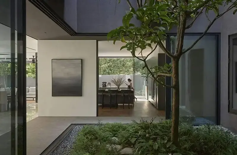 Courtyard with framed artwork on a white wall and a dining area visible through glass